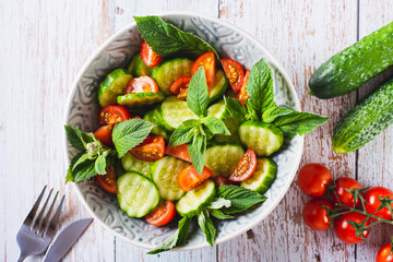 Close up of salad of cucumbers, cherry tomatoes and mint leaves in a bowl on the table top view