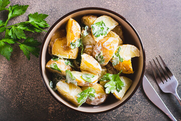Close up of potato salad in a peel with parsley and mayonnaise in a bowl on the table top view