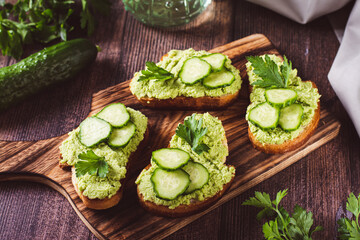 Crostini with avocado puree, cucumbers and herbs on a wooden board