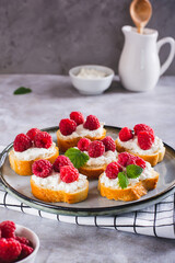 Appetizing crostini with ricotta, raspberries and mint on a plate on the table vertical view
