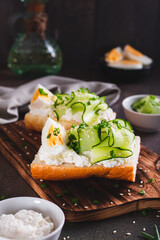 Sandwich with ricotta, cucumber slices, boiled egg and sesame seeds on a board vertical view