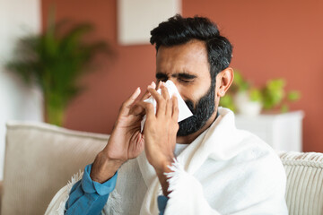 Arabic guy sneezing blowing runny nose in tissue at home