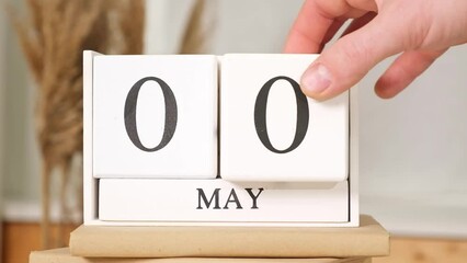 The man puts the date May 1 on the calendar. May 1st. may 1 wooden calendar on the table. Spring day. International Workers Day.