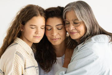 Calm adult, elderly and teenager women and daughter with closed eyes hugging