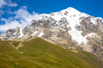 landscape of green grass and snowy mountains. Trekking and travel in Georgia
