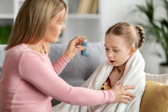 Preventing Attack. Caring mother giving asthma inhaler to sick child at home