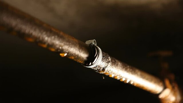 A male plumber puts a metal clamp on a water pipe. A man in the basement, repairing a water pipe from leaking.