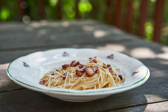 Vintage Rustic Plate With Delicious Spagetti Carbonara, Simple Traditional Recipe From Italian Cuisine Made From Pasta, Bacon, Eggs And Cheese, Served Outside In Garden Restaurant On The Wooden Table.