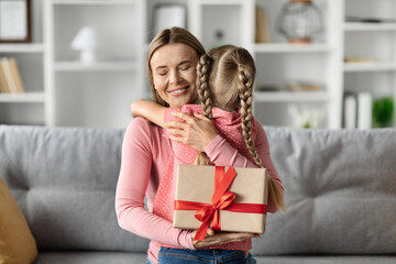 Cheerful young mother with gift box hugging her luttle daughter at home
