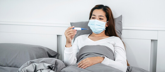 Asian woman in medical face mask feeling sick and holding thermo