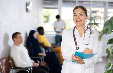 Young woman in medical uniform making notes in notebook at reception