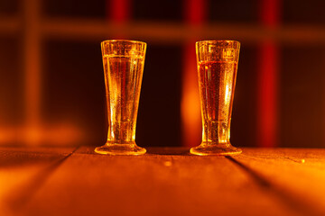 Two old vintage shot glasses with slivovitz on the old wooden table illuminated by orange candle lights. Picture is taken in the dark during hot summer midninght outdoor on the terrace of old house.
