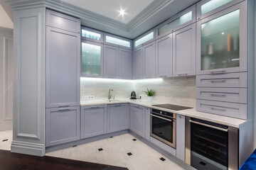 Elegant kitchen interior with light blue kitchen set. Hanging cabinets with glass doors and lighting.
