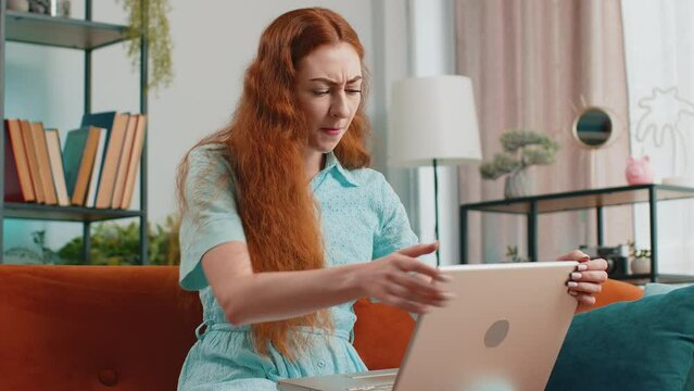 Displeased woman use laptop notebook typing browsing working, loses becoming surprised sudden lottery results bad news fortune loss fail computer virus. Redhead girl at home in room on couch