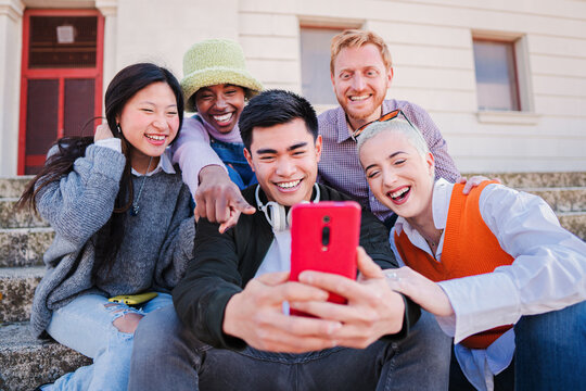 Group of multiracial best firends faving fun using a smartphone. Young people smiling and watching the social media app on a cellphone. Happy buddies browsing online on internet with a mobile phone