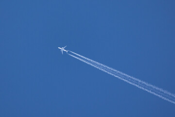 An airplane crossing the blue sky leaving a white trail of steam.
