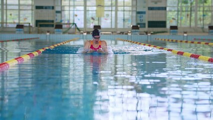 Slowmotion of professional competitive female swimmer swimming breaststroke in the indoor lap pool, front view. Swim technique concept.