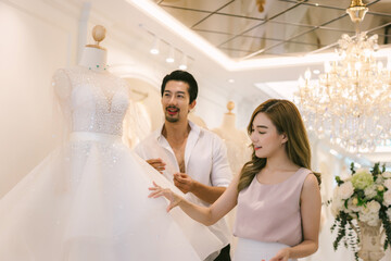 Naklejka premium Bride and groom choosing wedding dress in shop. Bride and groom choose dress and try to fitting in modern wedding studio.
