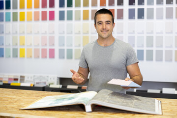 Man consultant of paintwork material department with samples and product catalog at counter and...