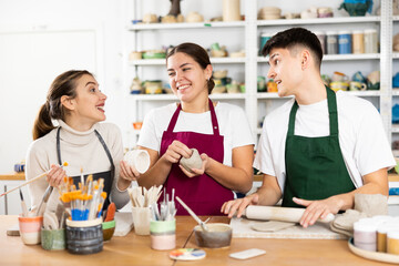 Fototapeta premium Two young women and young man sculpt pottery in workshop