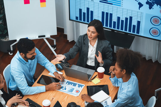 Top view multiracial analyst team use BI dashboard data to analyze financial report on meeting table. Group of diverse business people utilize data analysis by FIntech for business decision. Concord