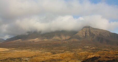Fototapeta premium Betancuria National Park on Fuerteventura Island, Canary Islands, Spain. Spectacular view of the picturesque desert nature landscape. The tops of the mountains are covered with white clouds, fog