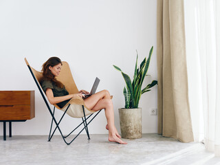 Woman sitting in a chair with a laptop watching a movie and social media at home smile, modern...