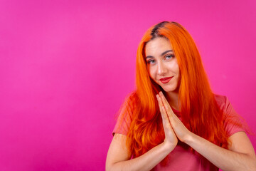Redhead woman in studio photography making the gesture please on a pink background