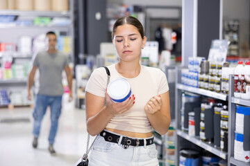Focused positive young girl planning to make house renovation, looking for paints in store. DIY...