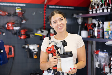 Woman examines handheld wireless portable spray gun, airbrush in tools department of construction...