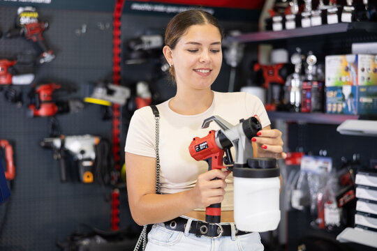 Smiling young woman involved in crafts or hobbies using of paint, choosing air sprayer in local hardware store