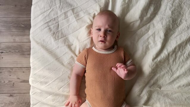 Funny baby boy lying on back near bed side looking at camera. Emotional adorable six months old infant,child smiling, having fun.Safety and care concept