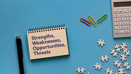 There is notebook with the word strengths, weaknesses, opportunities, threats. It is as an...