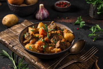 Irish stew made with beef, potatoes, carrots and herbs in a plate with cutlery on black background