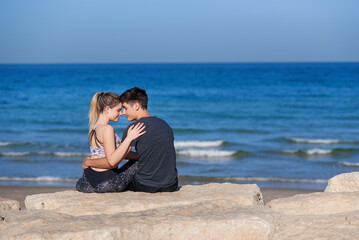 Young couple in love sitting on the rocky beach and looking on the horizon at sea.