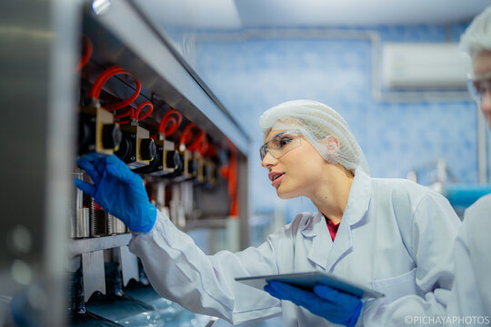 scientist worker checking the quality of water bottles on the machine conveyor line at the industrial factory. Female worker recording data at the beverages manufacturing line production. - Powered by Adobe