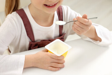 Cute little girl with tasty yogurt at white table, closeup