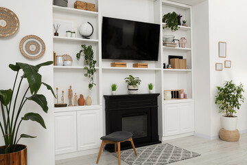 Stylish room interior with beautiful fireplace, TV set and shelves with decor and houseplants