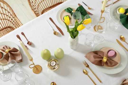 Festive Easter table setting with painted eggs, burning candles and yellow tulips indoors, view from above