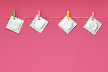 Clothesline with packaged condoms on pink background, space for text. Safe sex