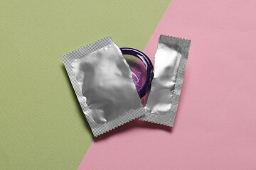 Condom in torn package on color background, top view. Safe sex