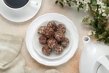 Delicious chocolate candies, cup of hot drink, teapot and blooming branch on beige table, flat lay