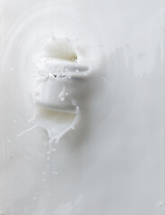 Cosmetic container white lotion droplet fly splashing. Milk lotion pour float to cosmetic bottle. Moisturizer lotion explosion spill. White background isolated high speed shutter freeze top view