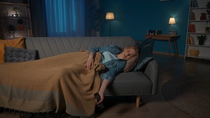 Tired sleepy woman fell asleep while watching TV. A woman sleeps, covered with a blanket, lying on...
