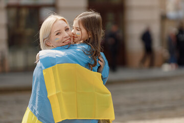Mother and her daughter hugging with a flag of Ukraine on a street