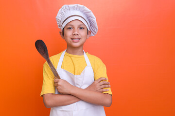 Smiling little boy chef holding spatula isolated on orange background with copy space. 