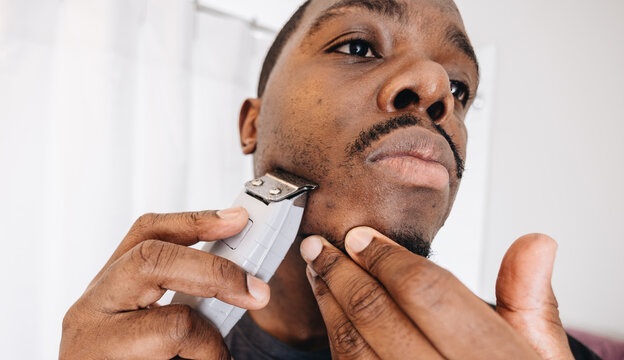 African American Man At Home In Bathroom Cutting Hair With Clippers