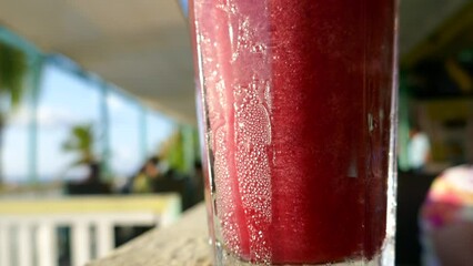 Frozen tropical drink with water drops from condensation in humid climate getting stirred with drinking straw
