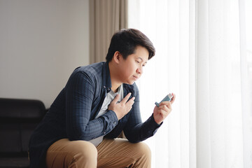 Sick Asian young man using inhaler to treat asthma and respiratory diseases at home. Asthma attack. Concept of allergy care. - obrazy, fototapety, plakaty