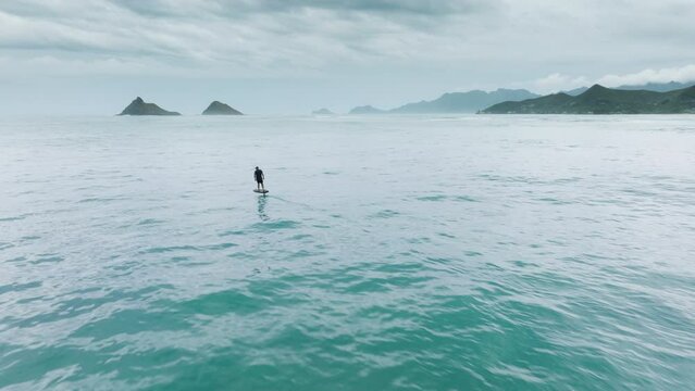 Athletic man rides a foilboard by using power of ocean waves. Water sport activity. Extreme sport activity shot on drone camera. Water sports on Oahu, Hawaii island. Surfer wake boarding on foil board